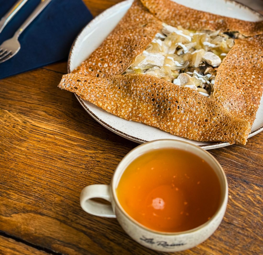 Une galette de sarrasin dorée servie avec une bolée de cidre breton sur une table en bois