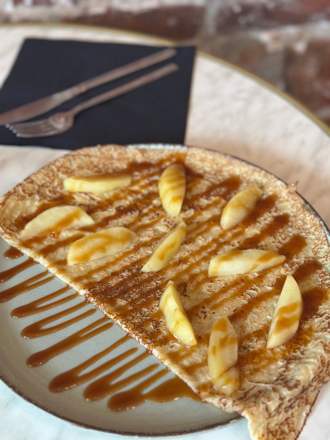 Une crêpe de froment pliée, garnie de quartiers de pommes et nappée de caramel au beurre salé, servie sur une table en marbre